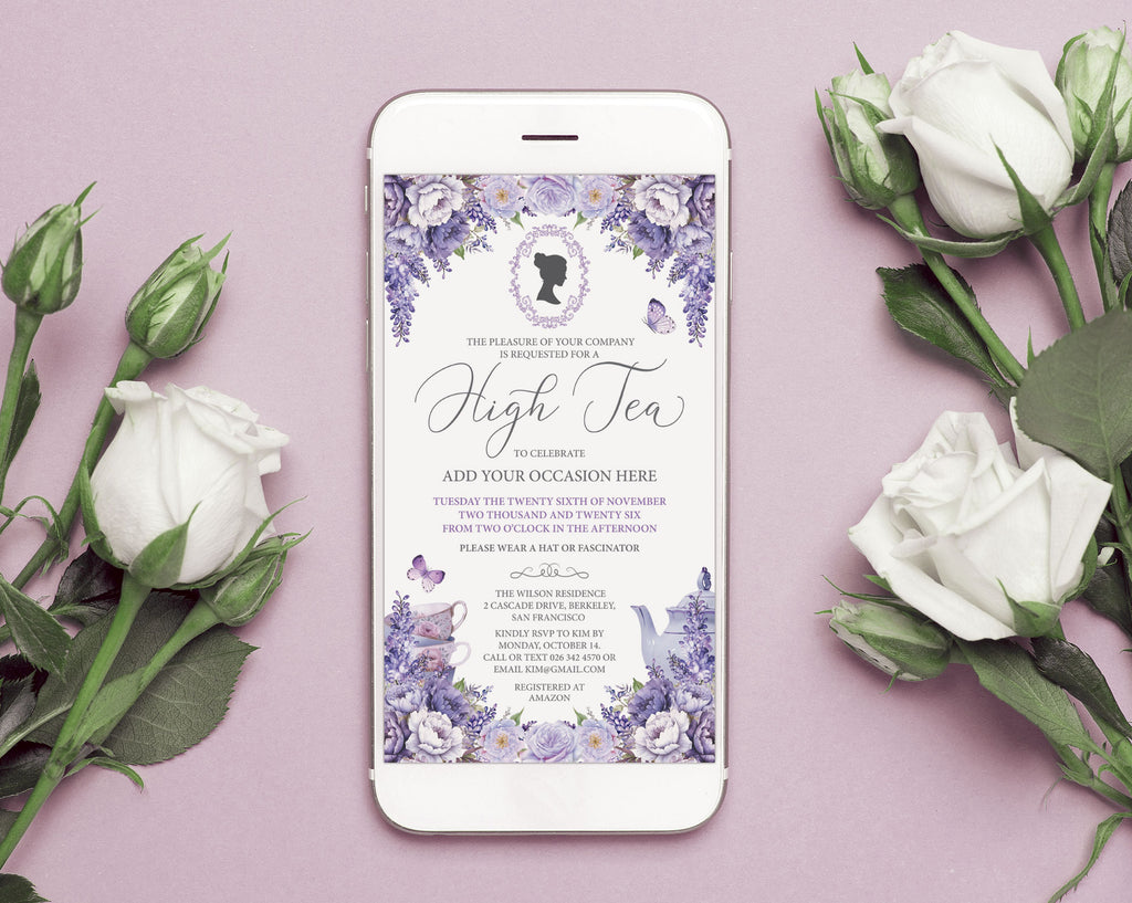 A white smartphone lying on a dusty pink background, surrounded by white roses and green stems. Screen displays a purple high tea invitation card with cameo, teapot and butterflies.