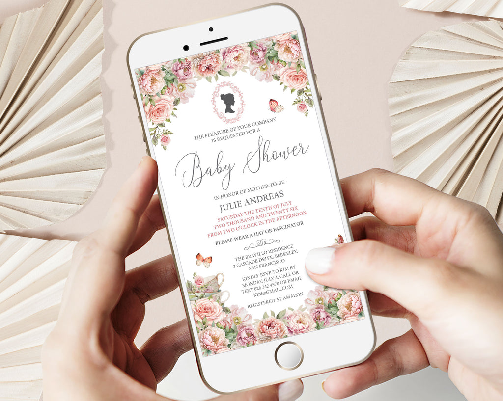 two hands holding a mobile phone with a blush pink flower regency style baby shower invitation showing on the screen, beige dried leaves in the background