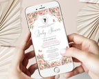 two hands holding a mobile phone with a blush pink flower regency style baby shower invitation showing on the screen, beige dried leaves in the background