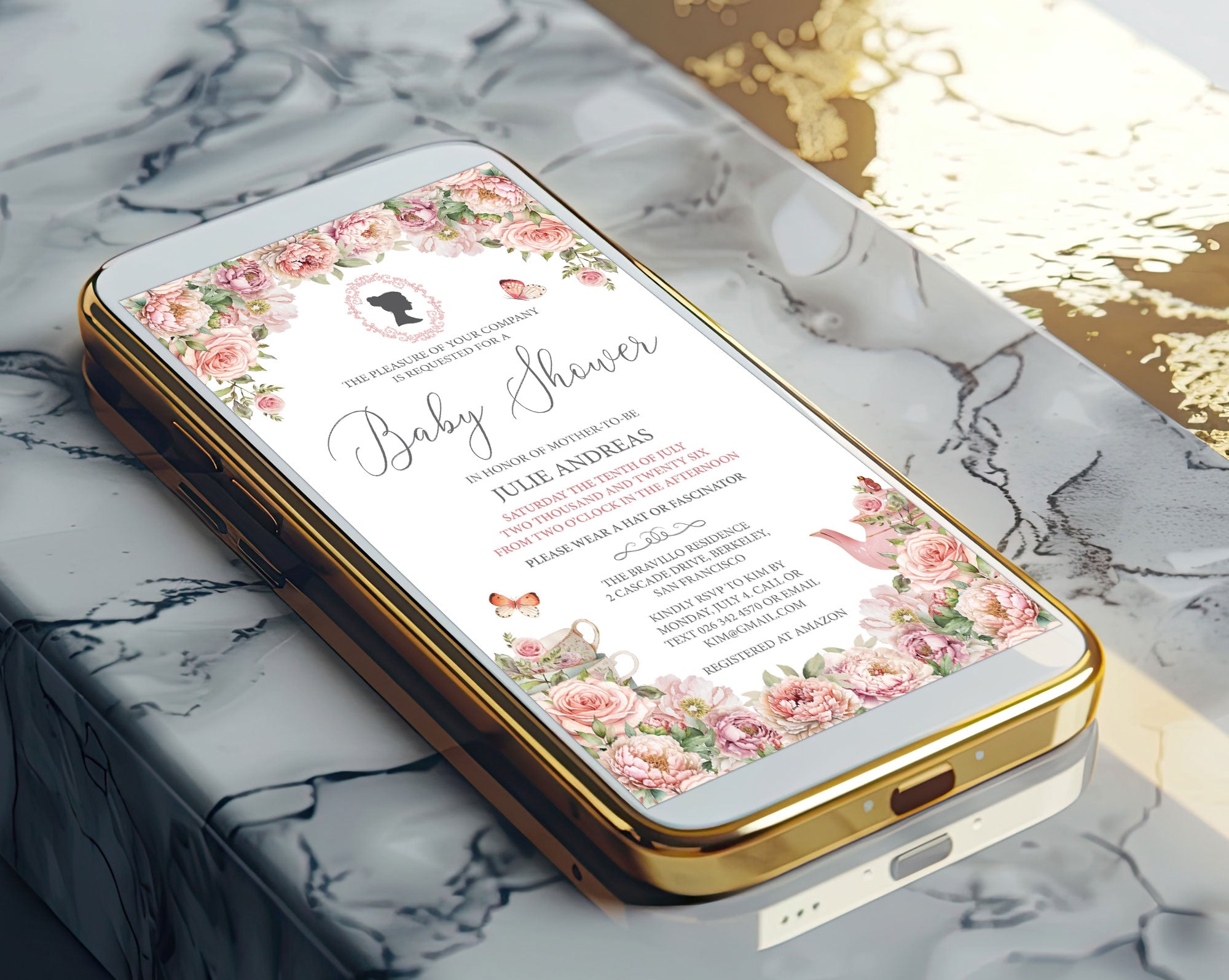 A gold mobile phone showing a pretty blush pink baby shower victorian style invitation on the screen laying on a marble surface