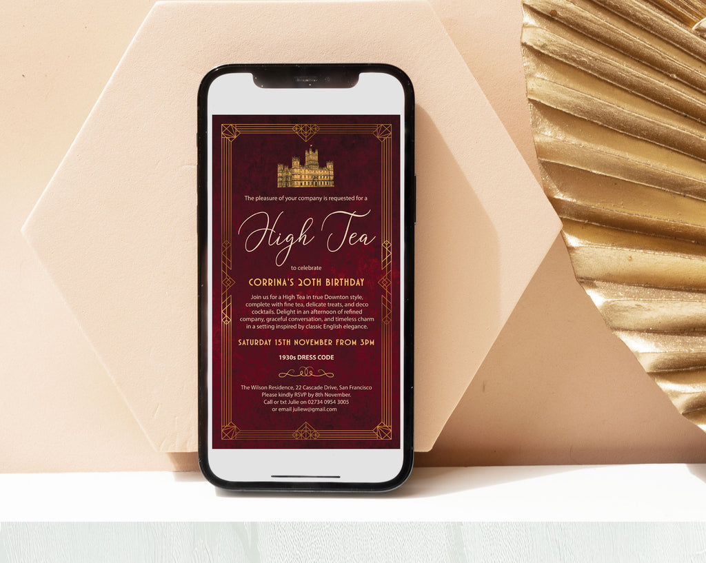 smart phone with an elegant burgundy and gold downton high tea invitation showing on the screen leaning against a beige wall next to a gold art deco leaf