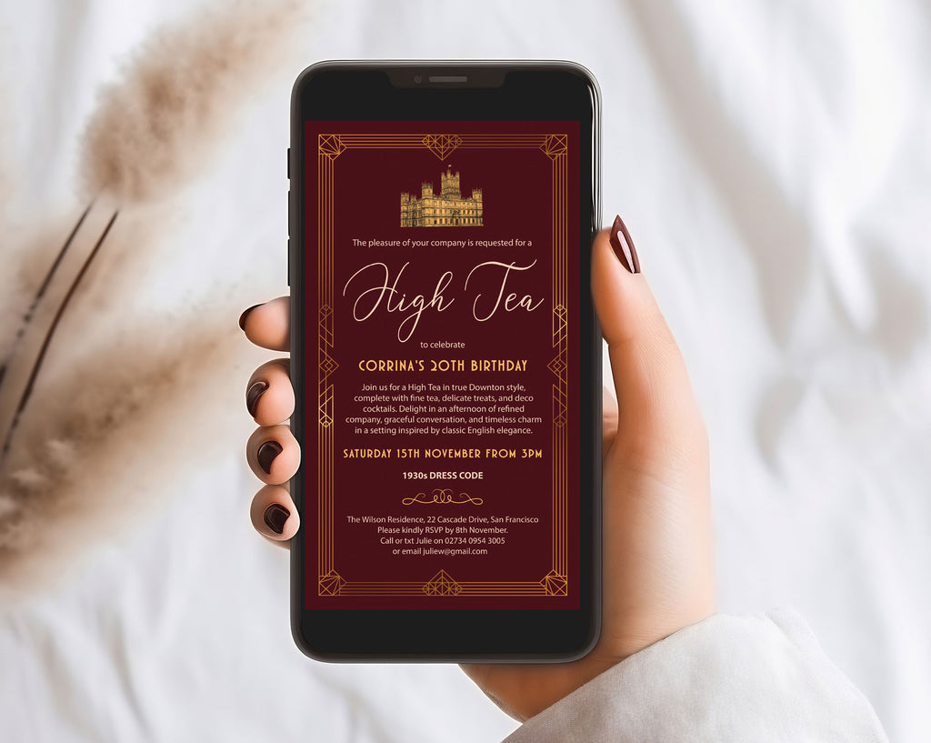 a hand holding a mobile phone with an art deco high tea burgundy velvet birthday invitation in front of a white cloth background