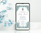 a black mobile phone with a dusty blue flower baby shower tea invitation showing on the screen, leaning up against a white wall with some blue blossoms