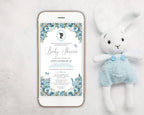 a dusty blue baby shower invitation showing on the screen of a white mobile phone, laying on a white background next to a stuffed rabbit with blue dungarees