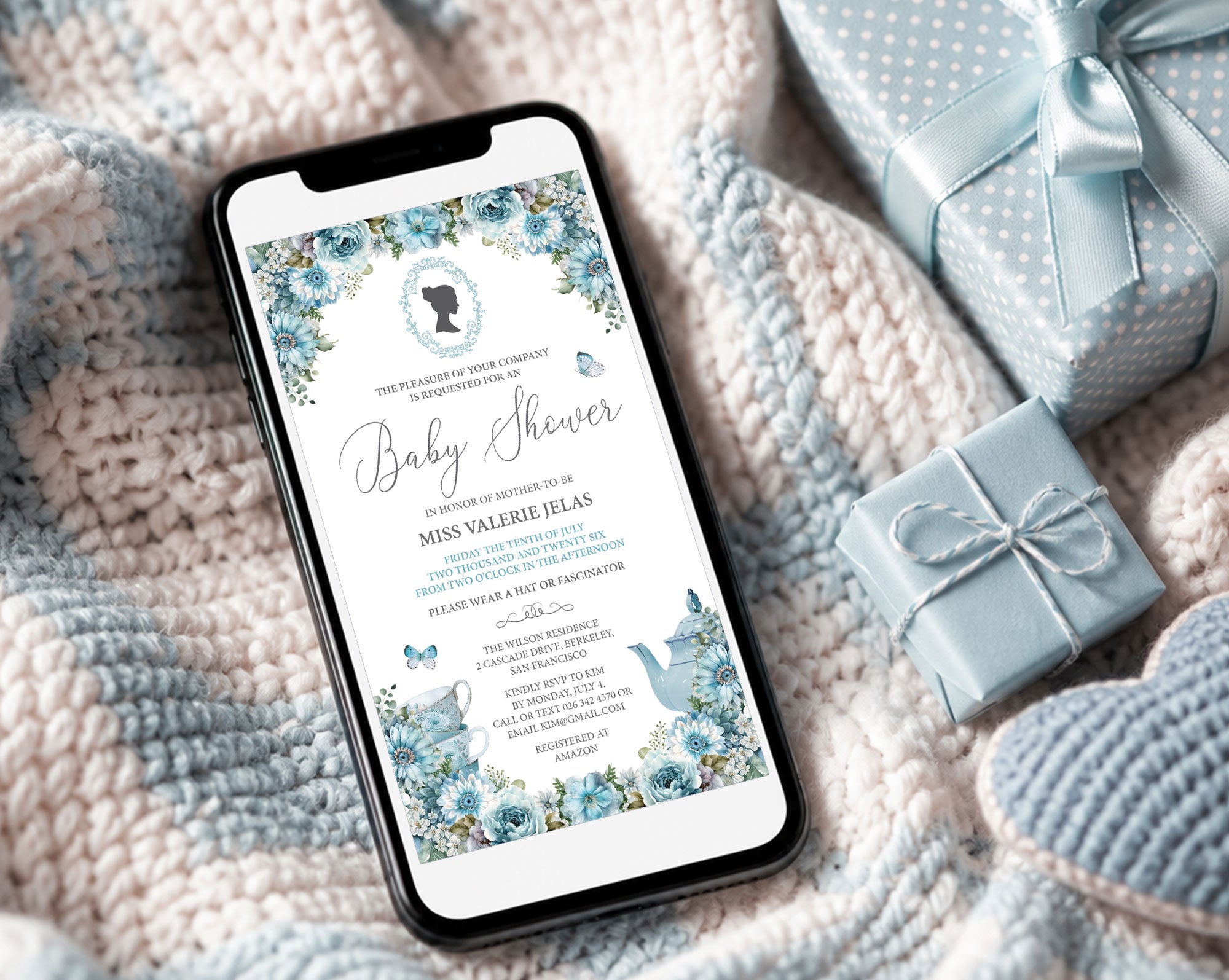 pretty blue regency style baby shower invitation showing on the screen of a mobile phone, laying on a baby blanket next to some blue wrapped gifts