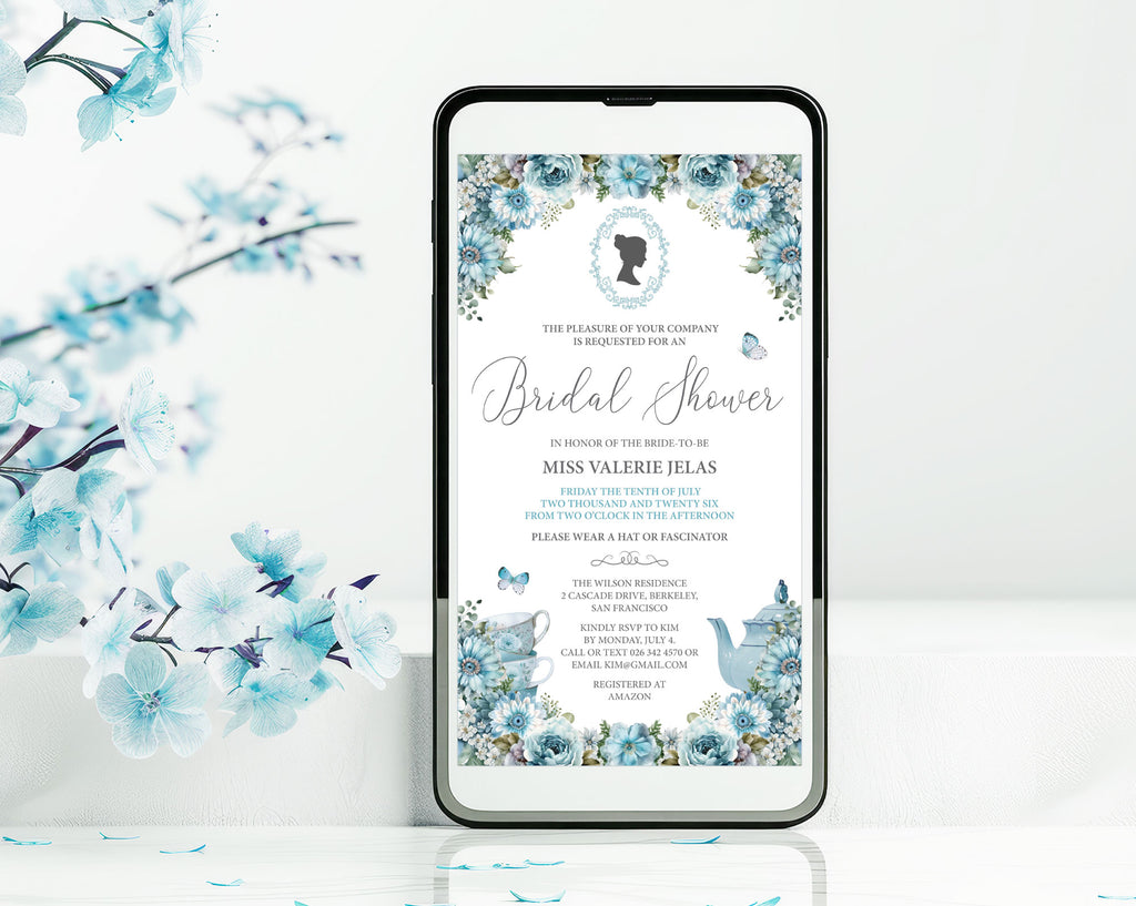 a black mobile phone with a dusty blue flower bridal shower tea invitation showing on the screen, leaning up against a white wall with some blue blossoms