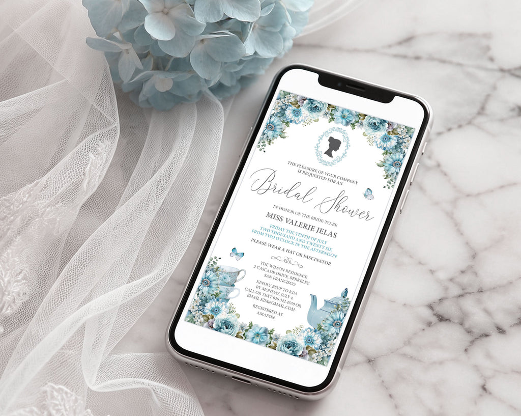 a black mobile phone with an elegant blue flower regency bridal shower invitation showing on the screen laying on a marble surface with a bridal veil and a blue hydrangea flower