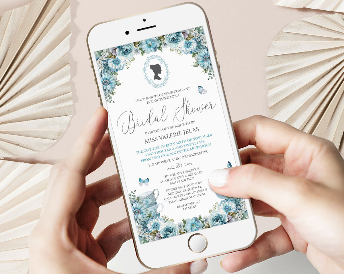 two hands holding a mobile phone with a dusty blue flower regency style bridal shower invitation showing on the screen, beige dried leaves in the background