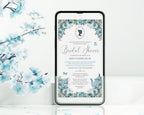 A smartphone mockup displays a dusty blue flower regency style bridal shower invitation. The phone is shown standing upright on a white surface with decorative blue blossoms in the background.