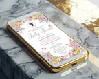 A gold mobile phone showing a pretty pastel baby shower victorian style invitation on the screen laying on a marble surface