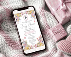 pretty pastel regency style baby shower invitation showing on the screen of a mobile phone, laying on a baby blanket next to some pink wrapped gifts