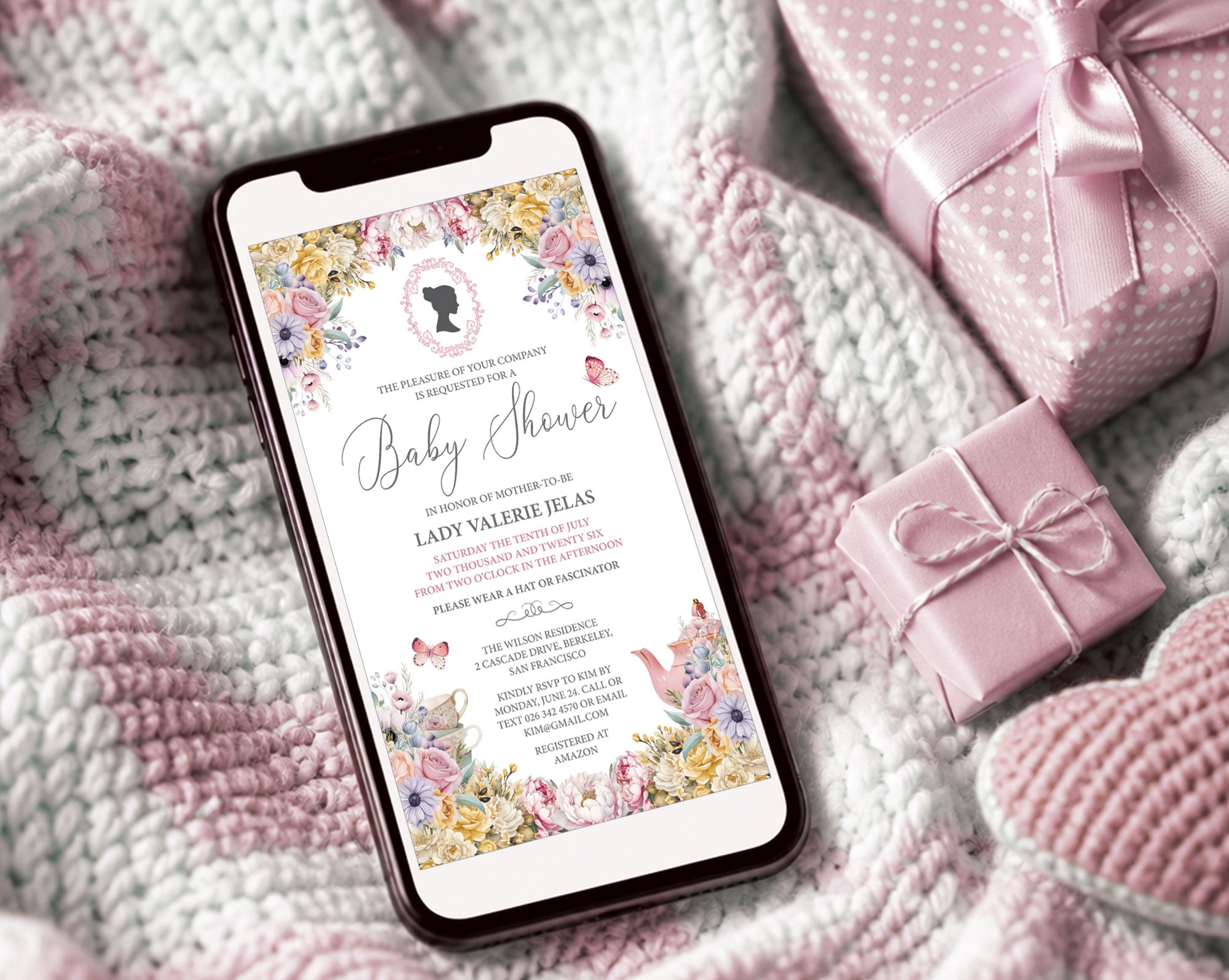 pretty pastel regency style baby shower invitation showing on the screen of a mobile phone, laying on a baby blanket next to some pink wrapped gifts