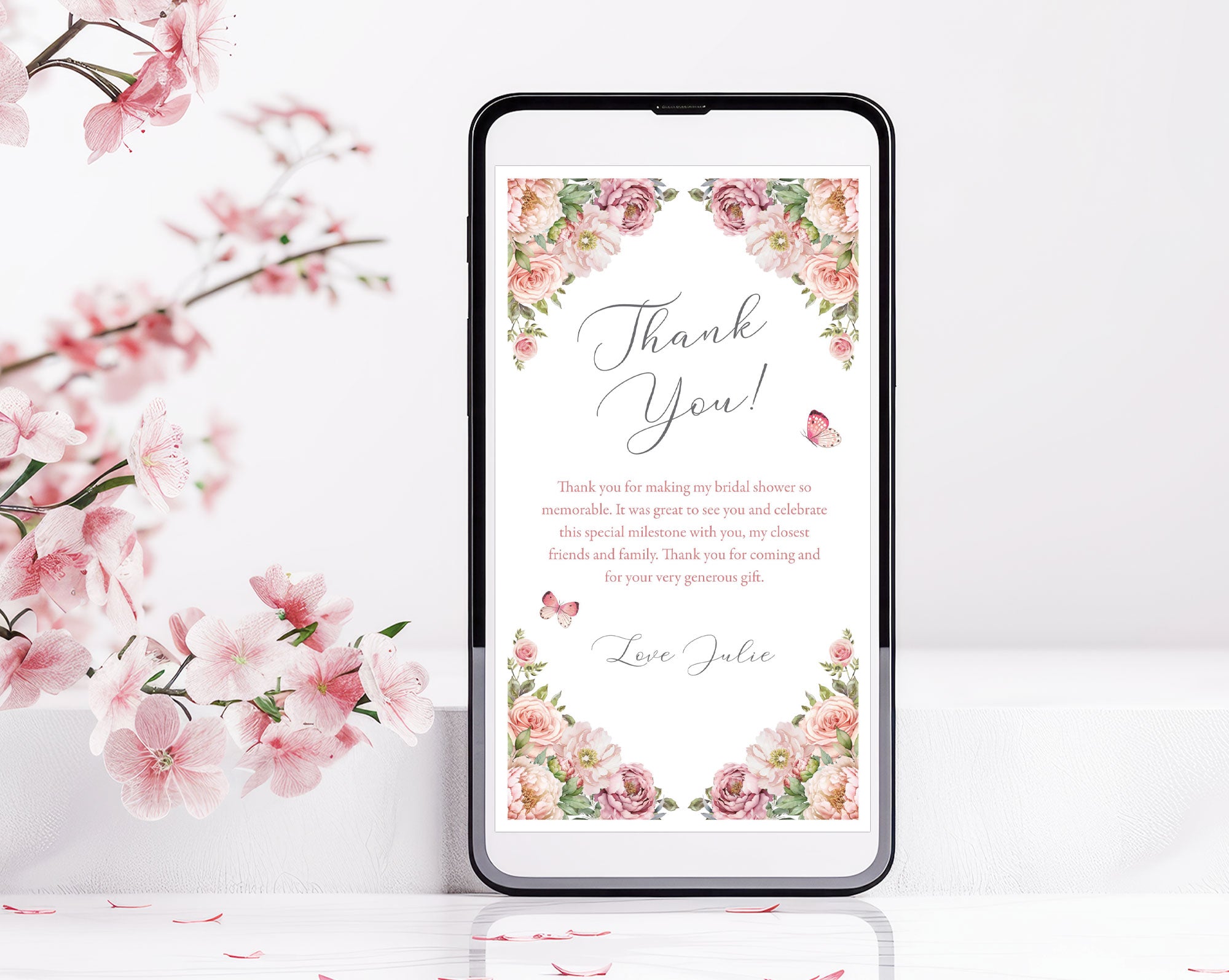 Phone screen displaying a floral 'Thank You' message standing upright next to cherry blossoms on a white background