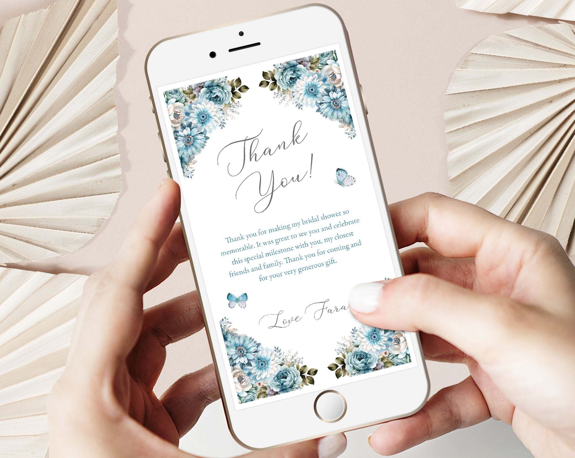 hands holding a mobile phone with a dusty blue flower Thank You note on the screen in front of a dried leaf beige background