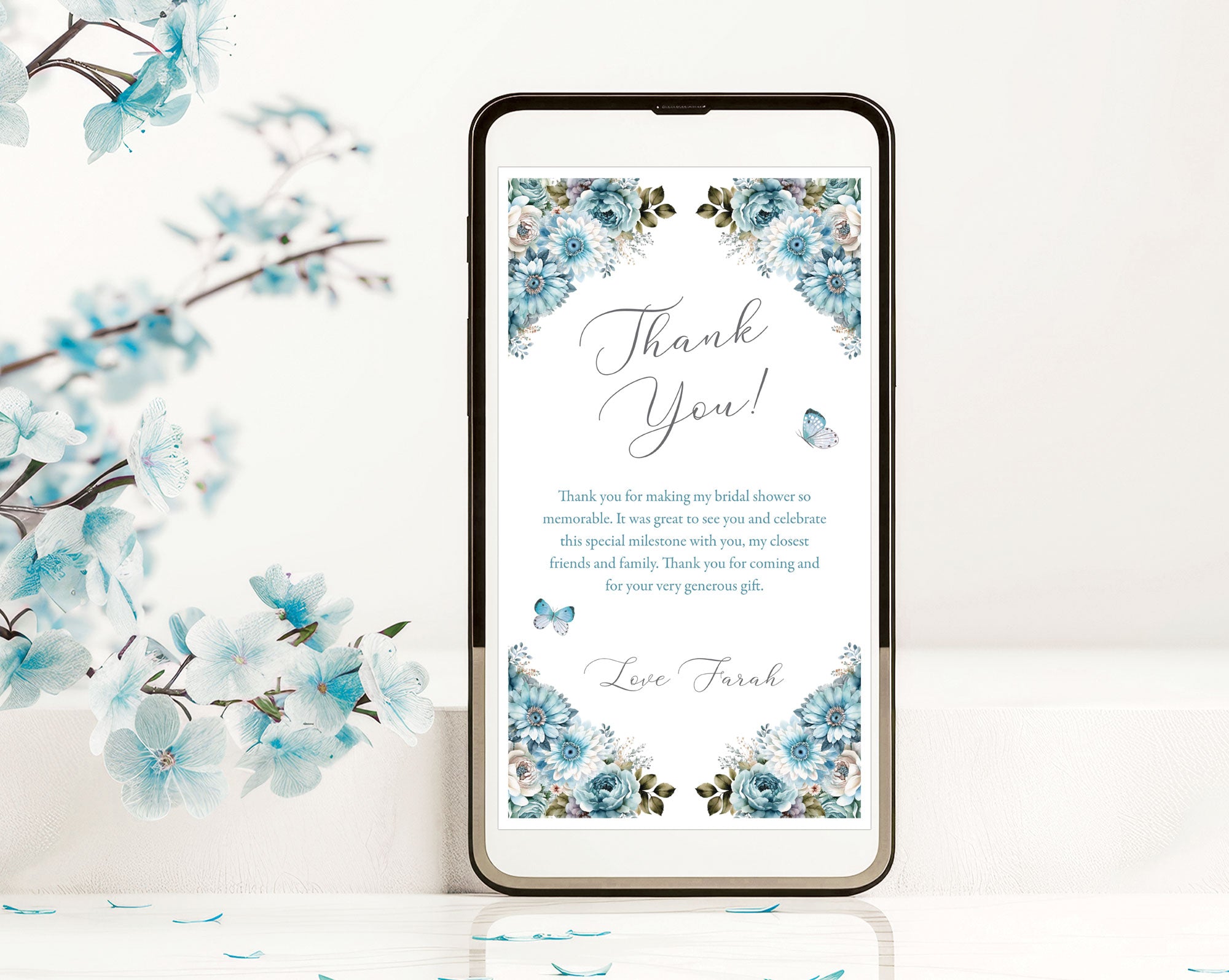 dusty blue thank you note with butterflies showing on the screen on a black mobile phone leaning against a white background next to some blue blossoms