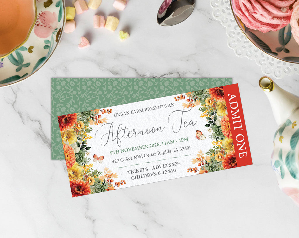 A printed tea invitation card with floral borders and event details, placed on top of a green patterned envelope on a white marble surface with tea and pastry props around it.