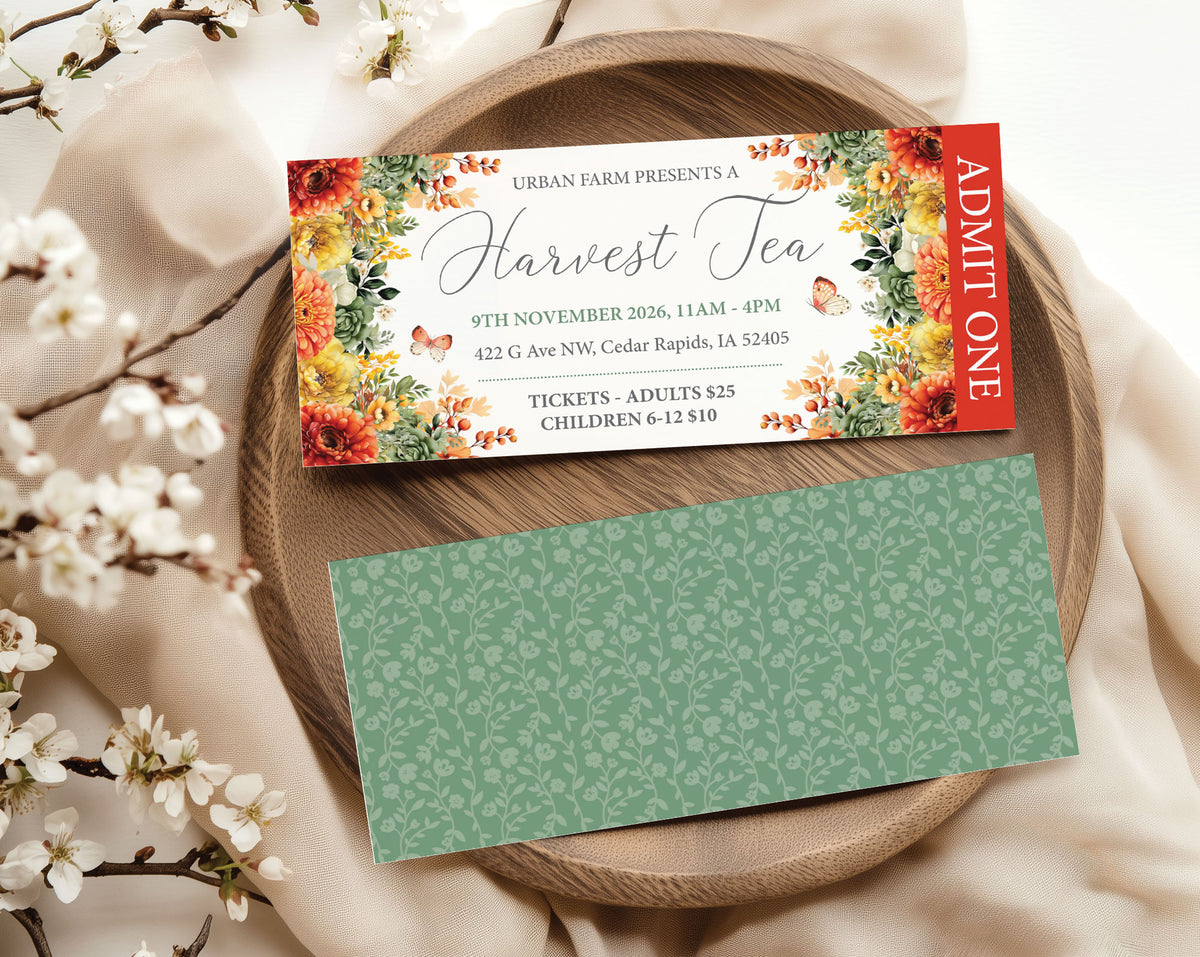 A printed event ticket for Urban Farm Presents Harvest Tea is displayed on a round wooden tray with a matching green patterned card underneath, surrounded by cream fabric and white blossoms.