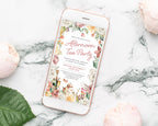 a pretty afternoon tea party invitation showing on the screen of a mobile phone that is laying on a marble surface next to some peach colored flowers