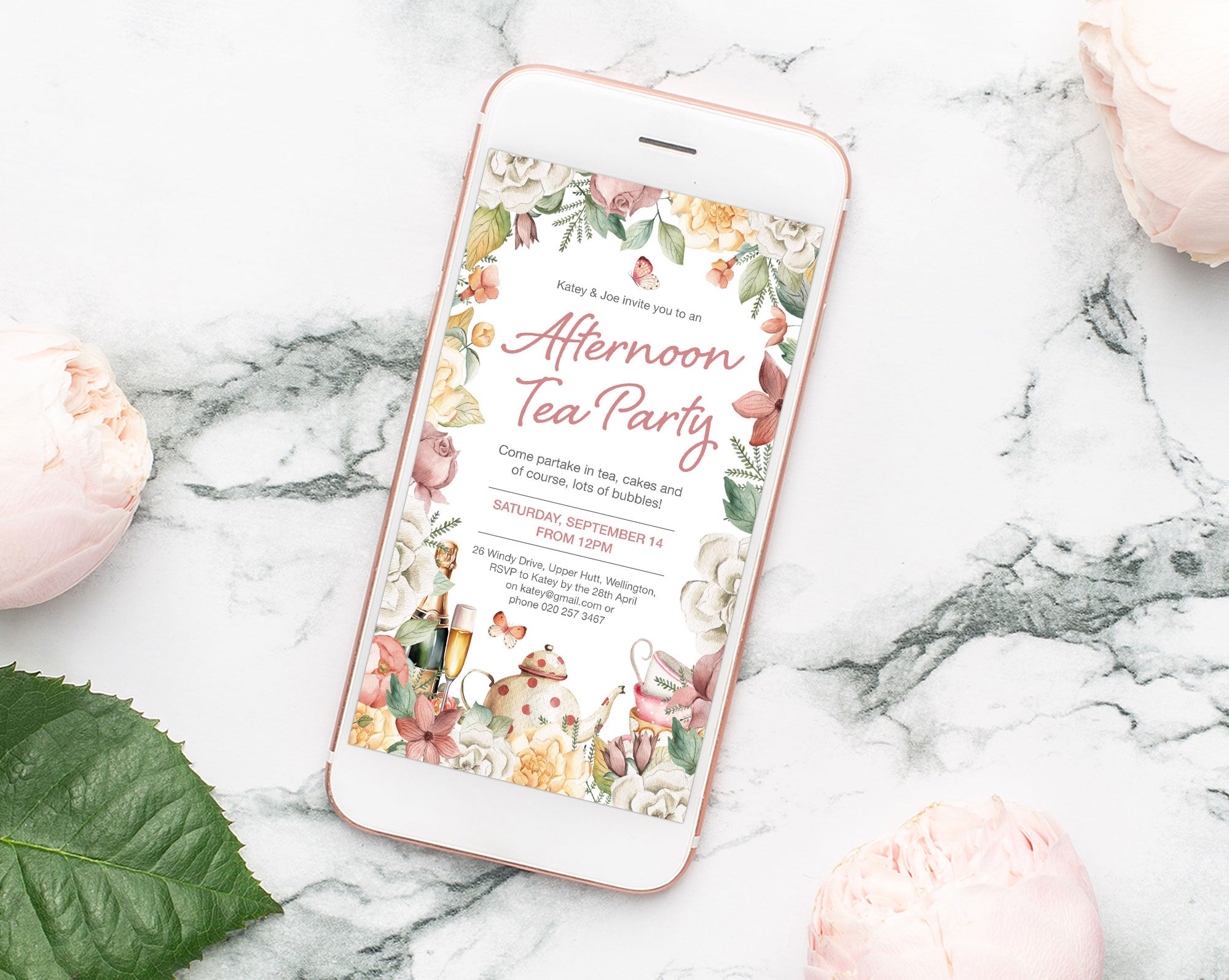 a pretty afternoon tea party invitation showing on the screen of a mobile phone that is laying on a marble surface next to some peach colored flowers