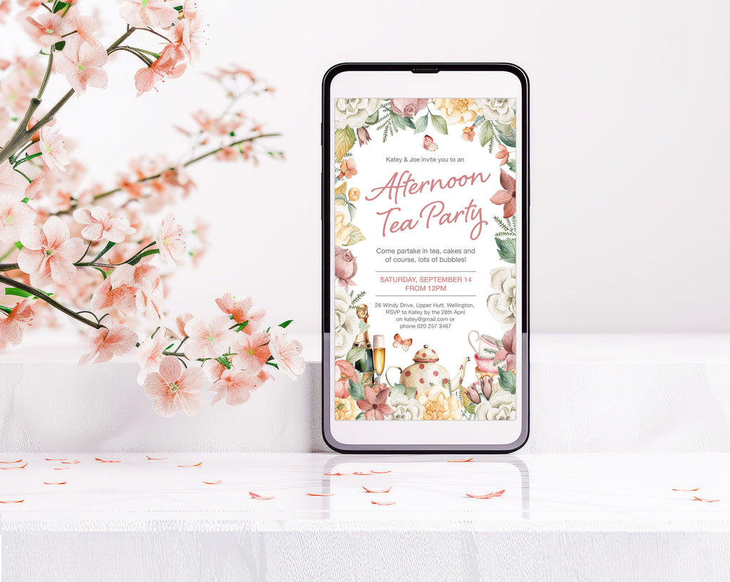 an afternoon tea party invitation with floral border and tea graphics showing on a black mobile phone next to some pink blossoms