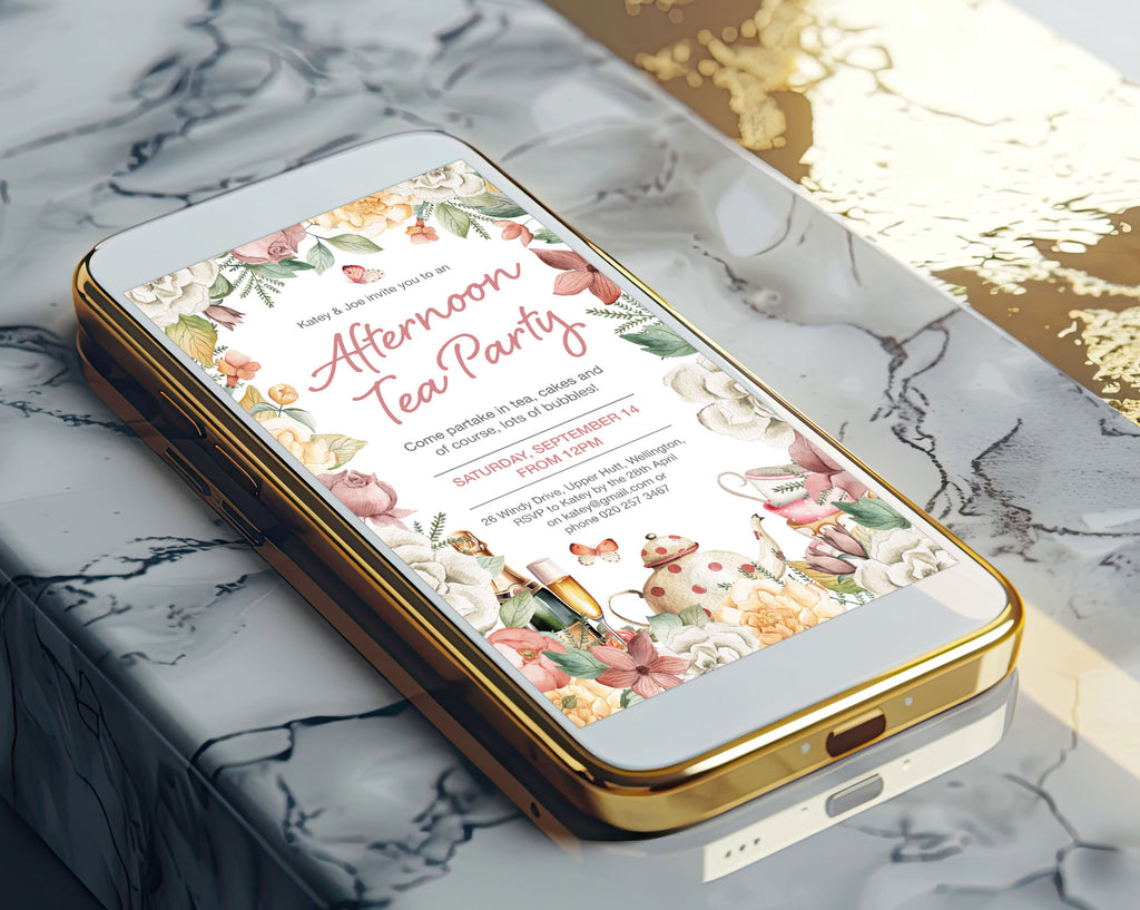 A gold mobile phone showing a Pretty floral afternoon tea invitation laying on a marble surface
