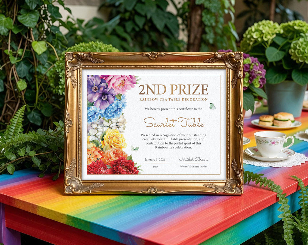 A framed certificate print with a gold ornate frame, displayed on a bright rainbow-colored table outdoors. The certificate is for a '2nd Prize Rainbow Tea Table Decoration' and features colorful floral illustrations on the left.