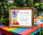 A framed certificate print with a gold ornate frame, displayed on a bright rainbow-colored table outdoors. The certificate is for a '2nd Prize Rainbow Tea Table Decoration' and features colorful floral illustrations on the left.