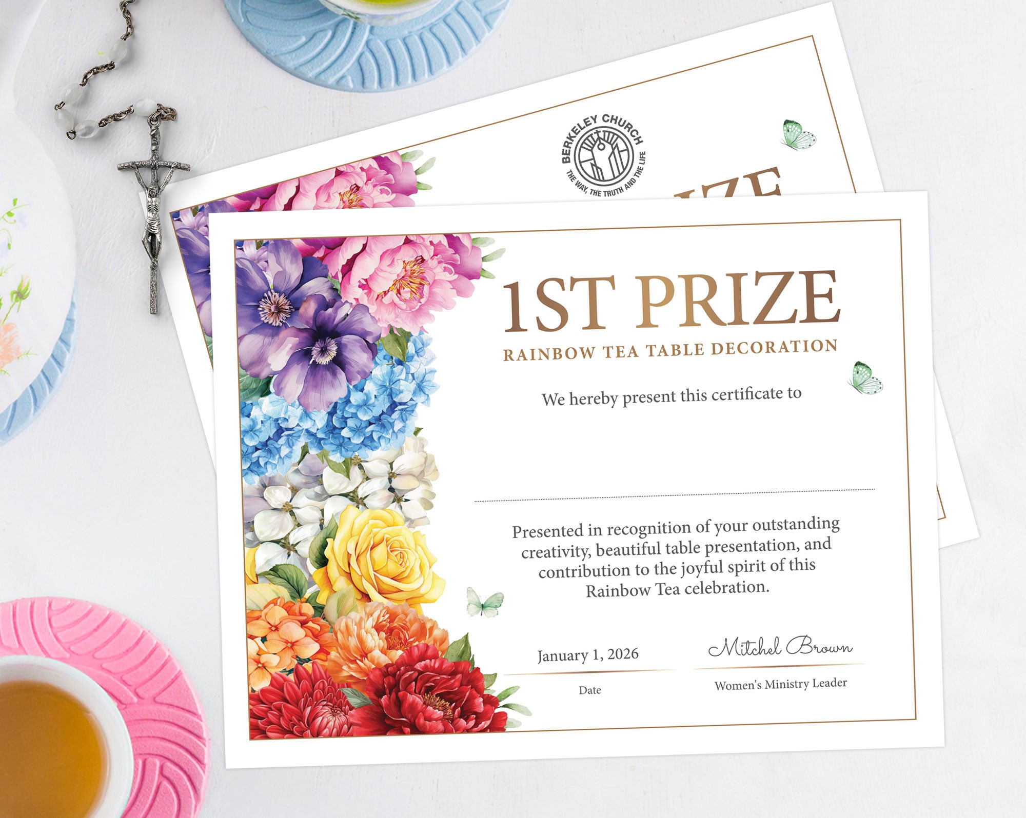 two rainbow tea 1st prize certificates with bright flowers and one with church logo, laying on a white table top with a tea service and a crucifix necklace next to them