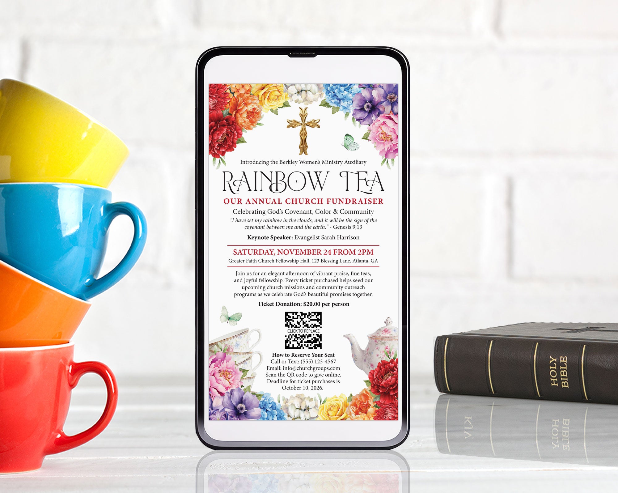 A smartphone centered on a reflective white surface, displaying a colorful church fundraiser invitation titled 'Rainbow Tea.' Surrounding the phone are stacked bright yellow, blue, and red mugs on the left, and a dark leather-bound Bible on the right, against a white brick wall background.