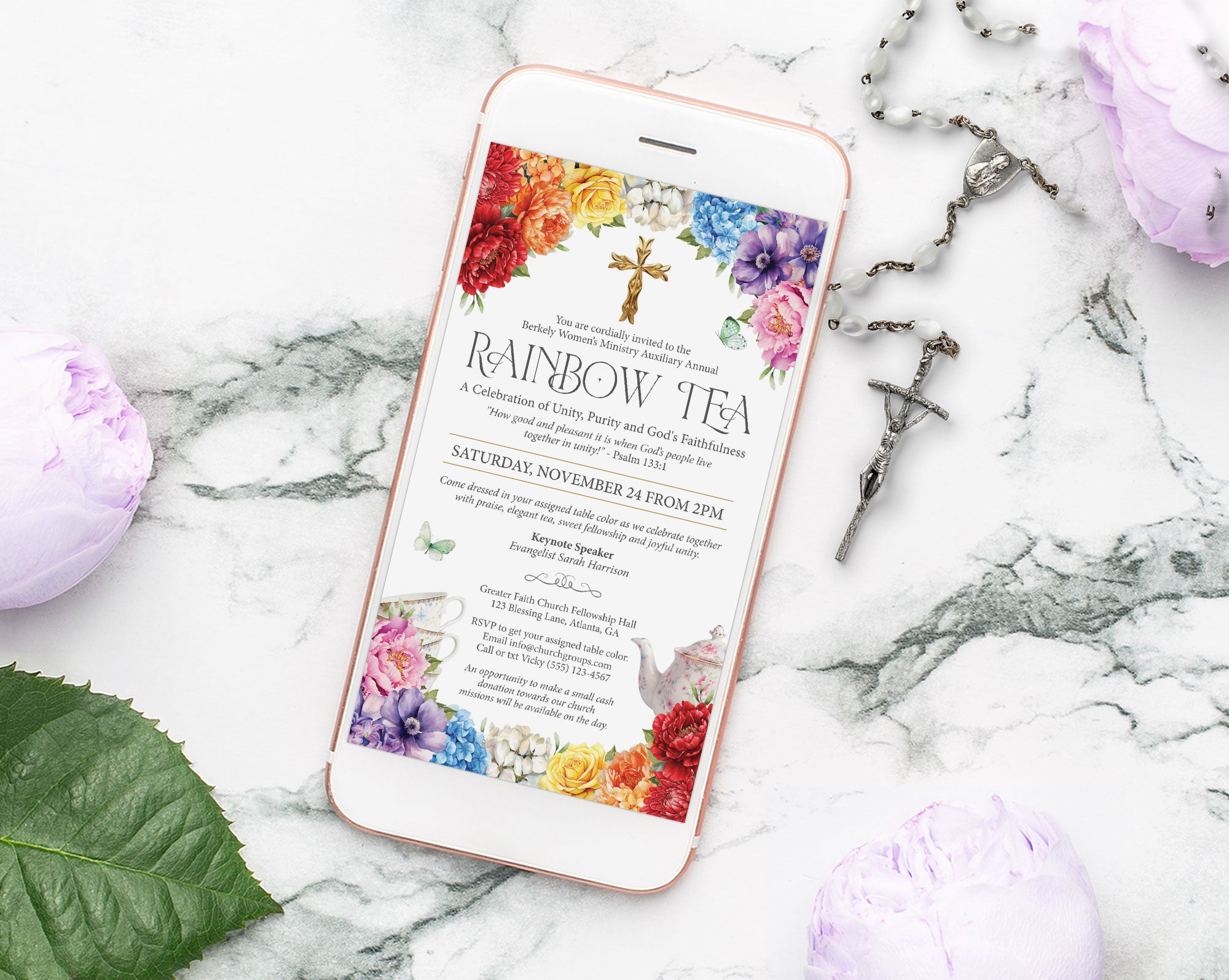 a white mobile phone with a colorful rainbow event invitation laying on a marble surface with a crucifix and some lilac flowers next to it