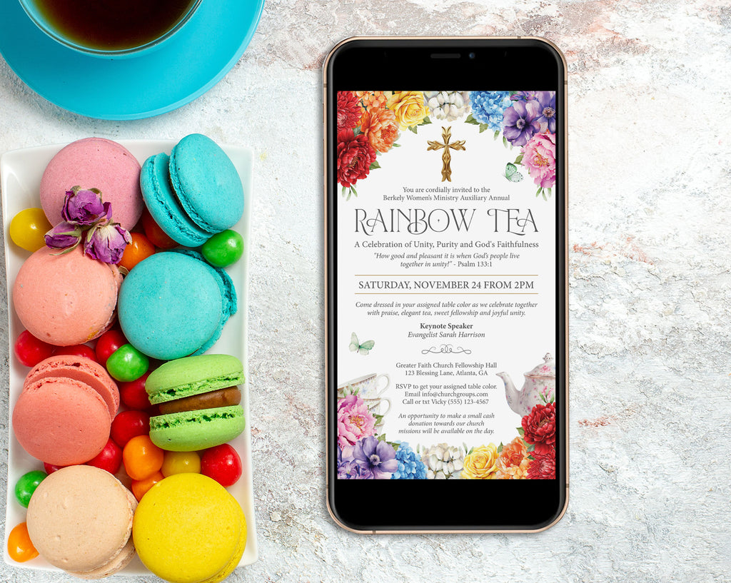 a black mobile phone showing a church rainbow tea invitation, laying on a marble surface next to a tray fill of colorful macarons and a blue tea cup