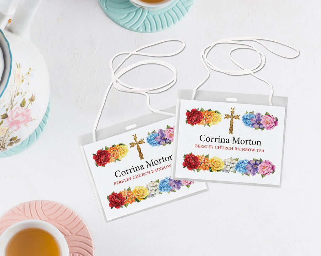 Two rainbow religious fundraiser tea hanging name badges in plastic covers with neck straps lying on a white background next to a pastel tea set