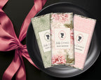 Three floral-themed baby shower favor chocolates on a black plate with a pink ribbon.