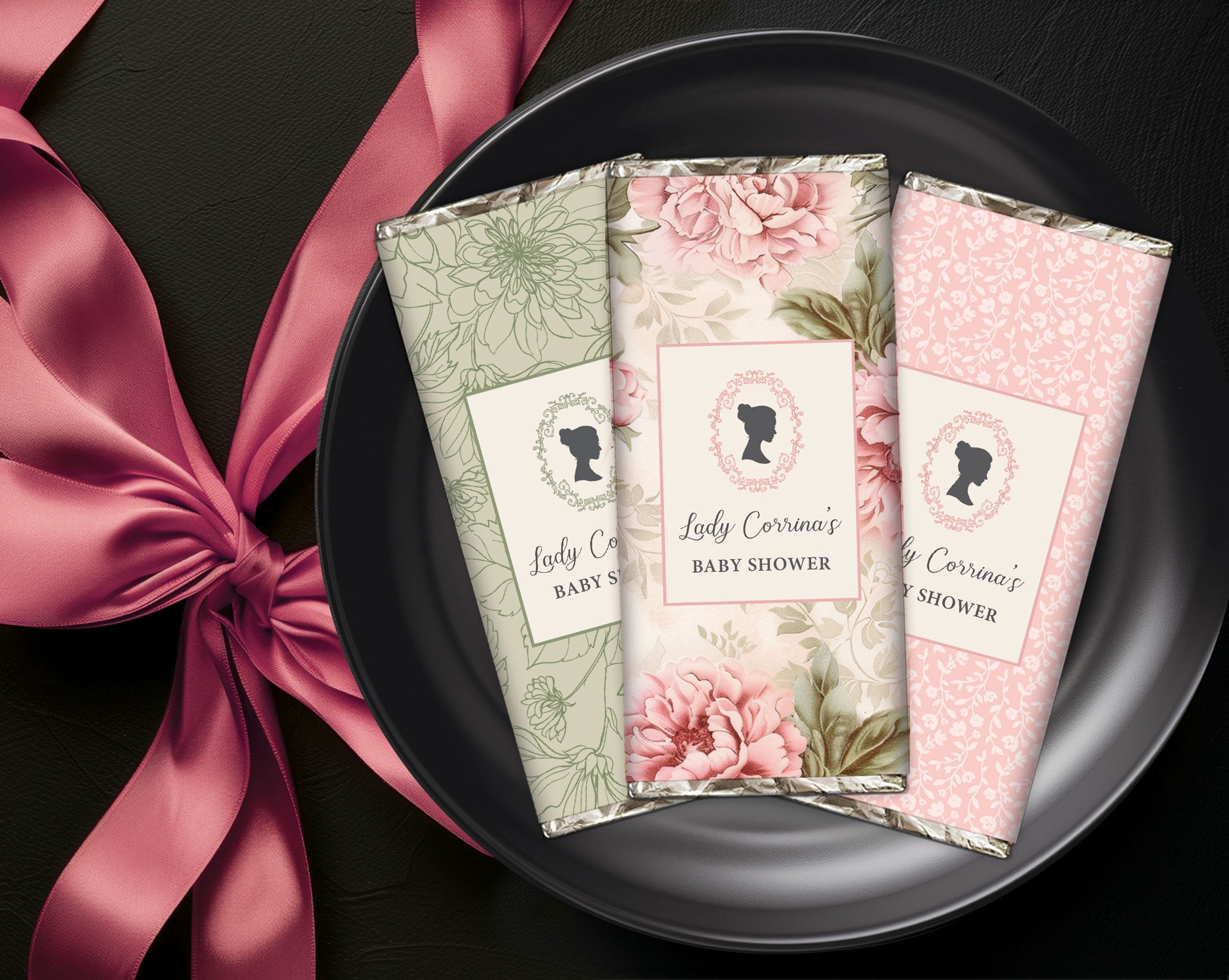 Three floral-themed baby shower favor chocolates on a black plate with a pink ribbon.