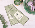Green floral-patterned chocolate bars with a cameo detail on a white wooden background with plate of macarons