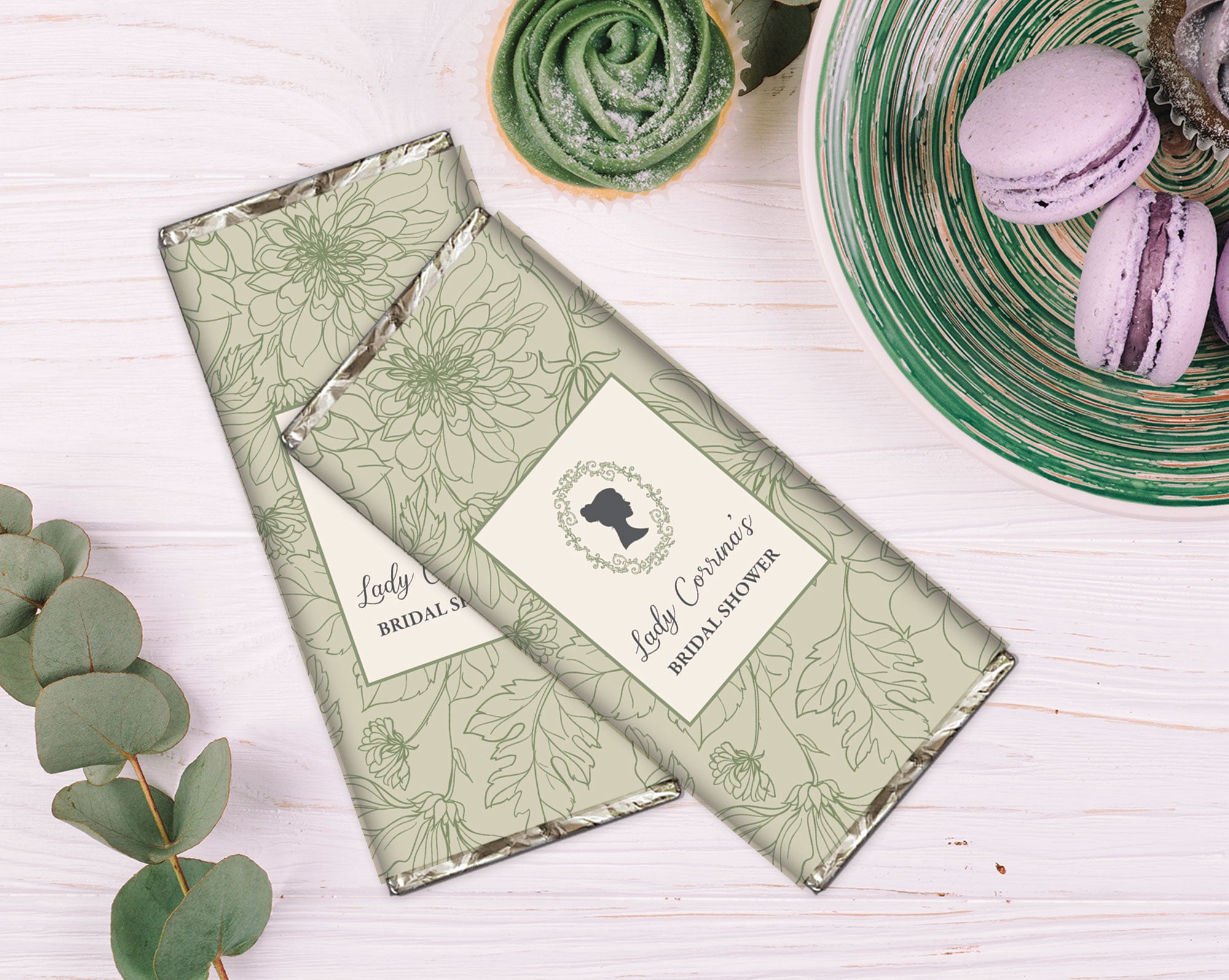 Green floral-patterned chocolate bars with a cameo detail on a white wooden background with plate of macarons