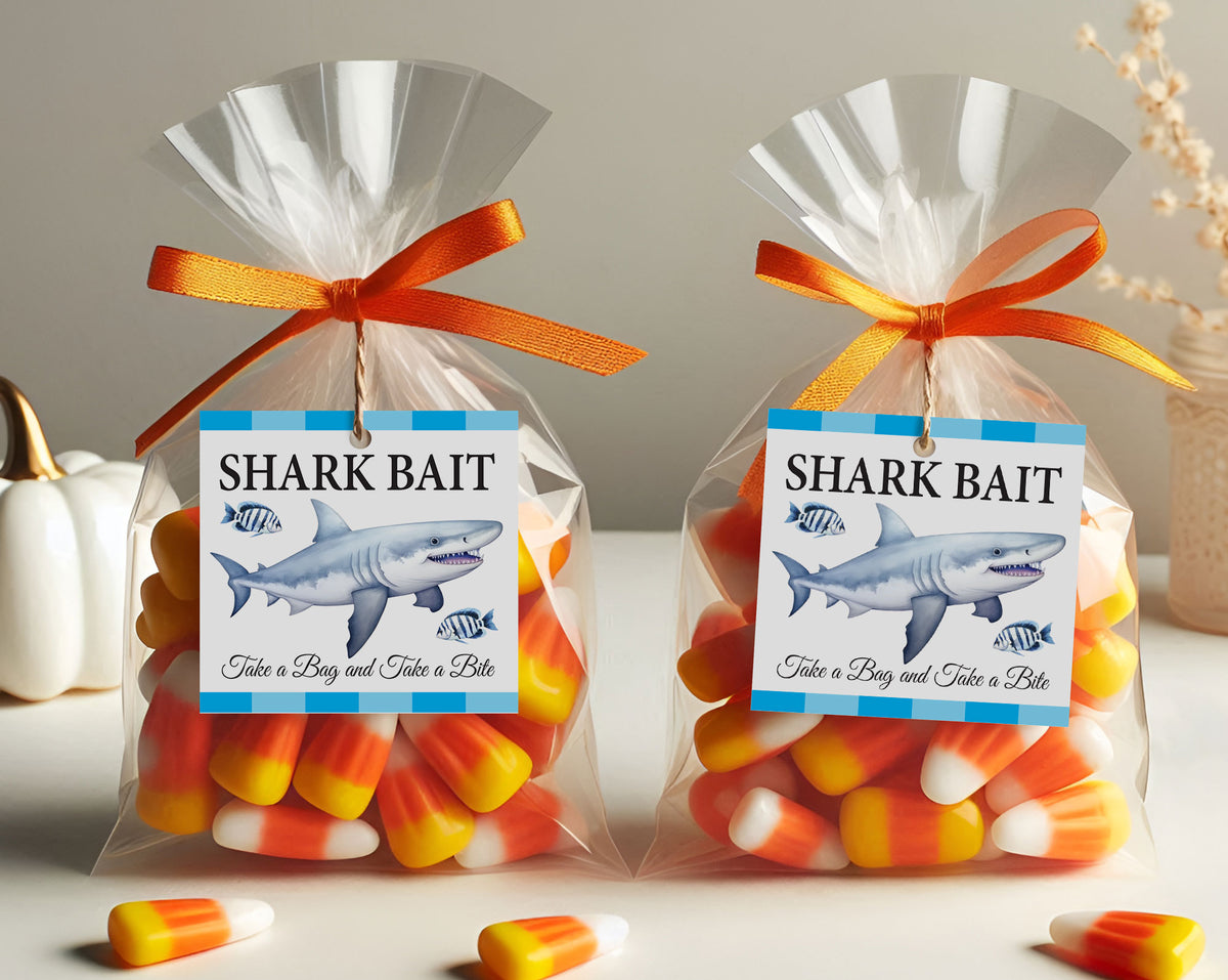 Two clear cellophane candy bags tied with orange ribbons and labeled "SHARK BAIT" with a shark illustration, filled with candy corn, on a tabletop with a neutral background.