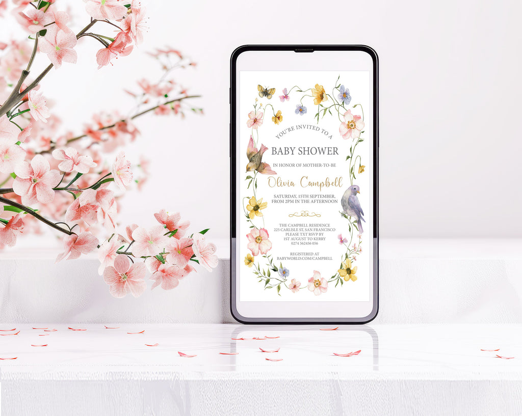 a baby shower invitation with floral border with bird graphics showing on a black mobile phone screen next to some pink blossoms