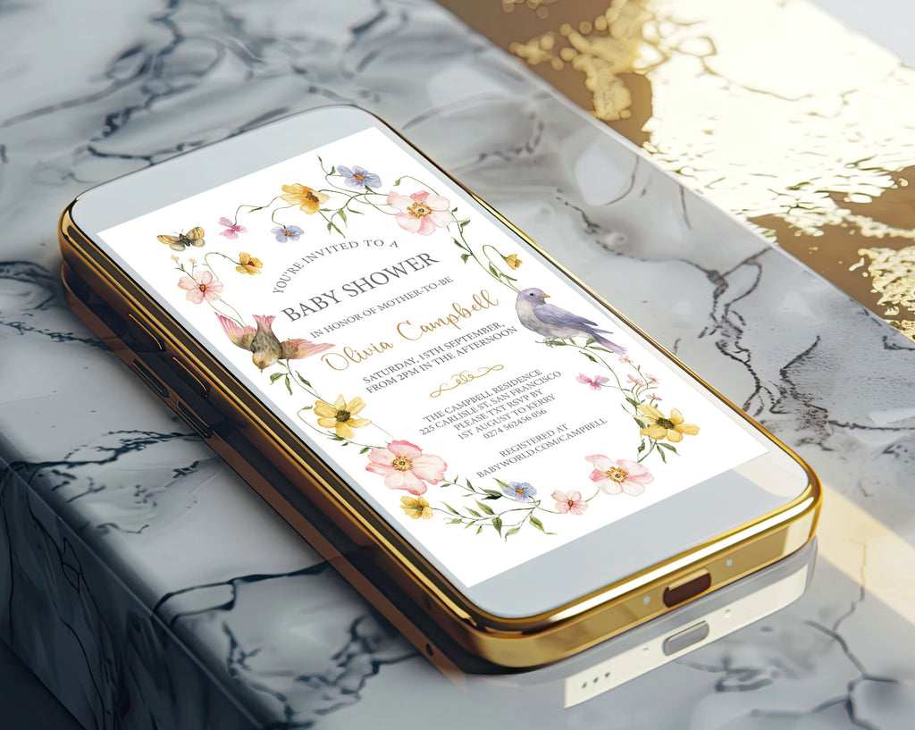 A gold mobile phone showing a pretty floral and bird baby shower invitation on the screen laying on a marble surface