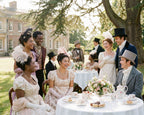 Pretty black ladies, white ladies and gentlemen dressed in regency period costumes at a tea party outside in front of a manor house