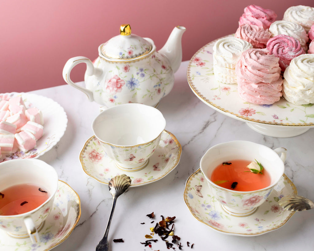 Tea set with floral teapot and cups on a marble surface with pink background