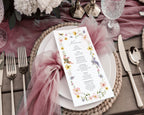 pretty baby shower menu with birds and wildflowers laying on a white plate on a pink gauzy cloth, on a wooden table set with cutlery