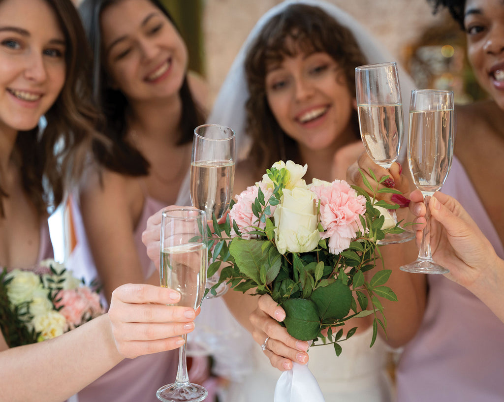 Bride with bouquet and bridesmaids holding champagne glasses, celebrating.